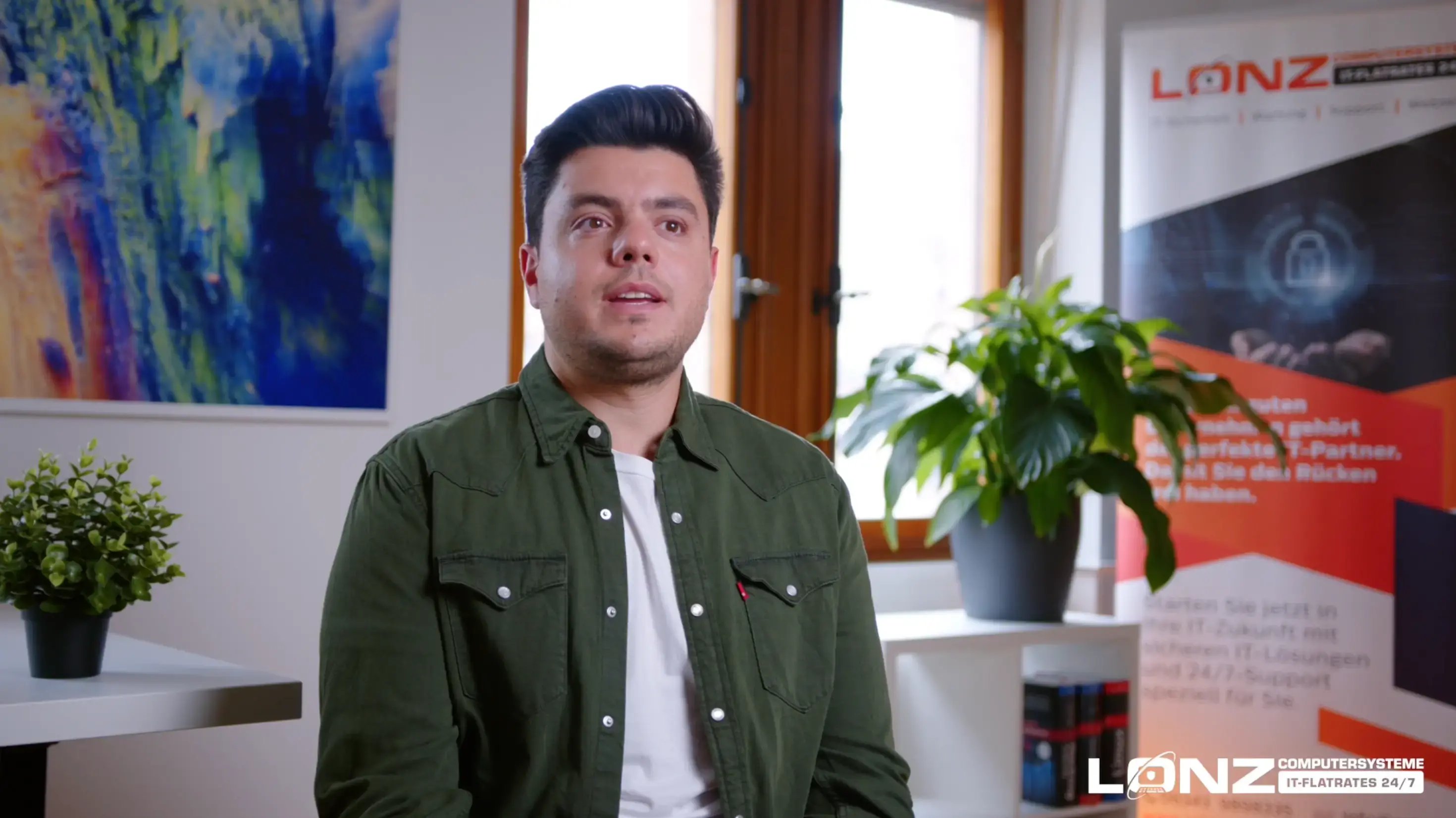 Video-Vorschaubild von Emanuel Lonz von ComputerSysteme Lonz. Er sitzt in einem Büro und spricht während eines Interviews, im Hintergrund ist das Werbebanner der Firma zu sehen.